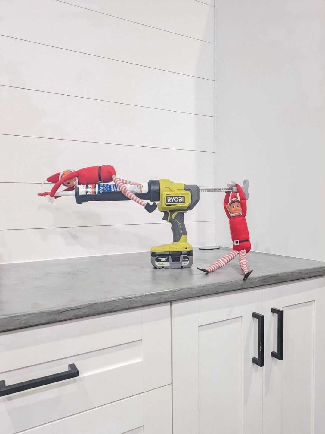 Lutins farceurs accrochés à un pistolet à silicone posé sur le plan de travail de la cuisine