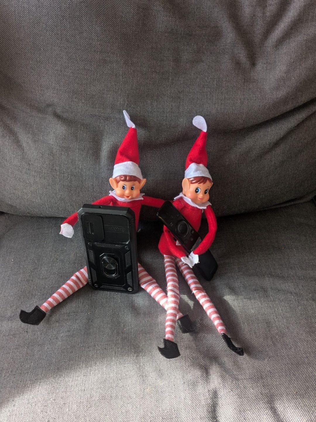 Deux lutins farceurs assis sur un canapé en train de regarder un écran de téléphone